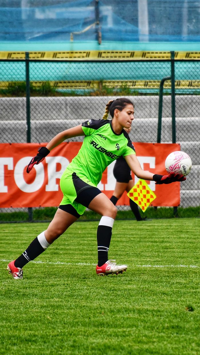 journey-01 Young woman saving a goal during a soccer game on a green field.