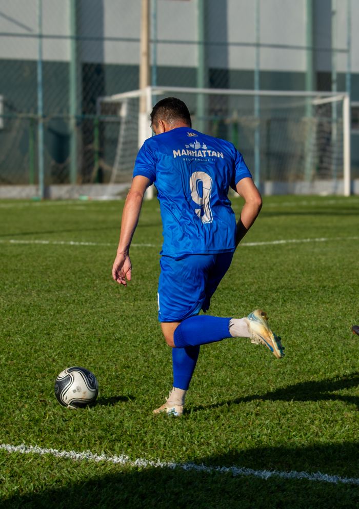 about-img Athletic soccer player in blue jersey kicks ball during daytime match on grass field.