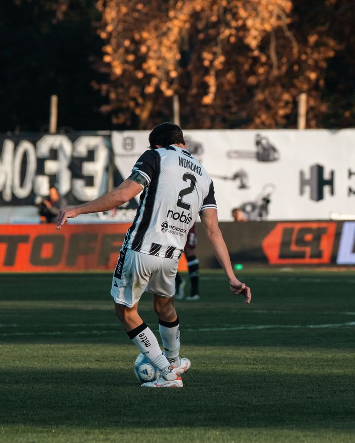 A soccer player kicks the ball during a competitive match under sunlight.