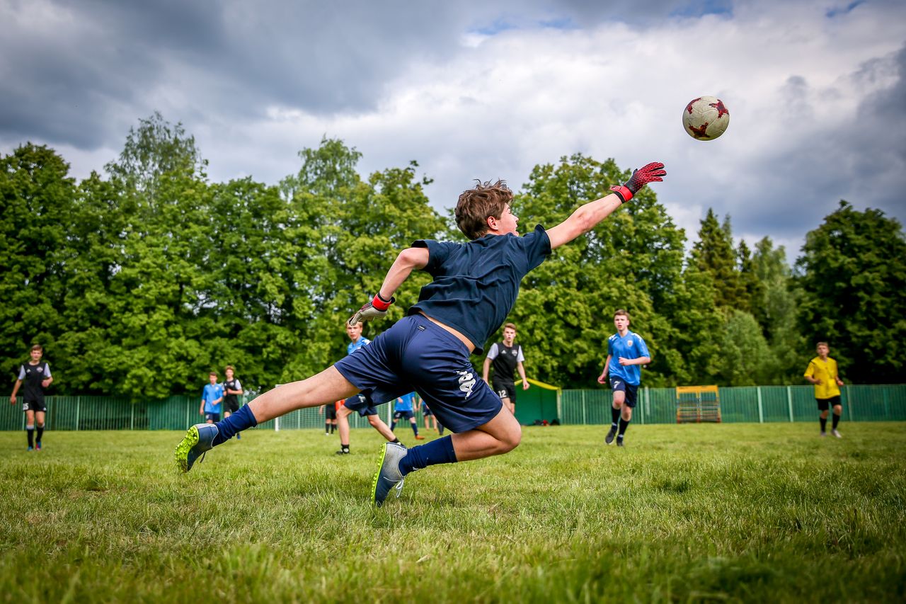 vision A young goalkeeper dives to catch a soccer ball during a lively outdoor game on a green field.