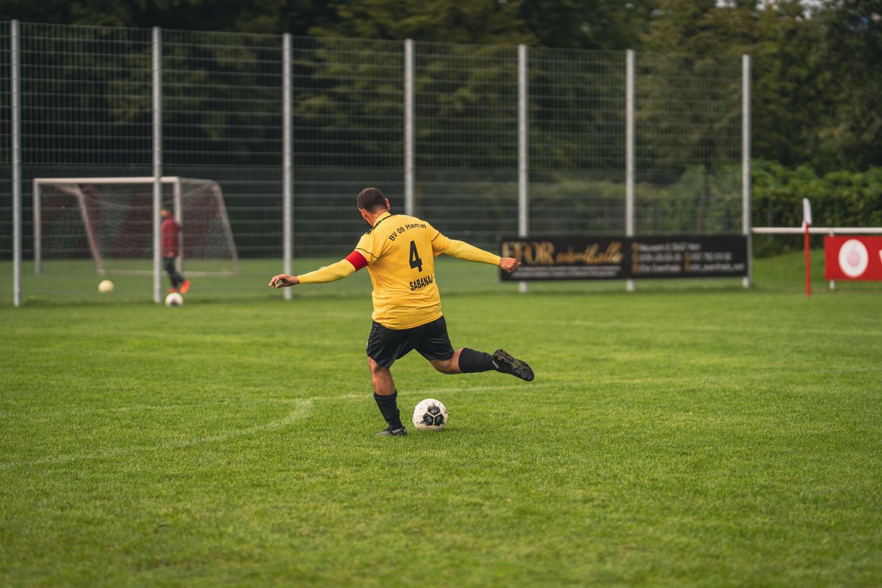 trusted-partner An amateur soccer player in yellow jersey kicks a ball on a grassy field during the day.